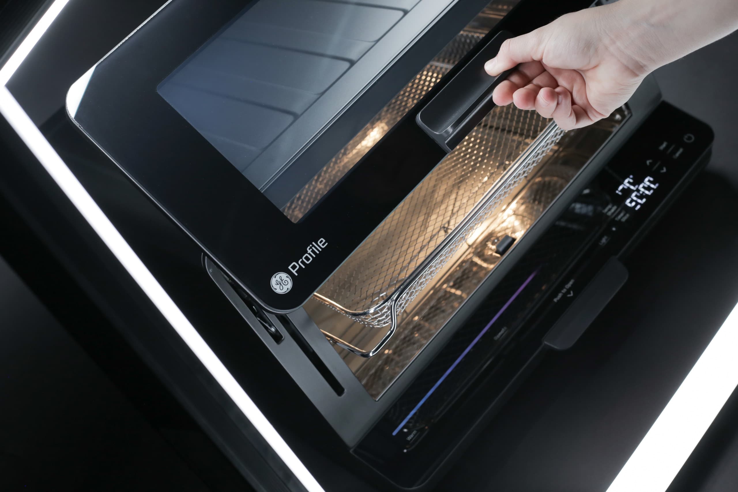 A hand opening the door of a modern GE Profile oven, revealing the illuminated interior and wire racks.